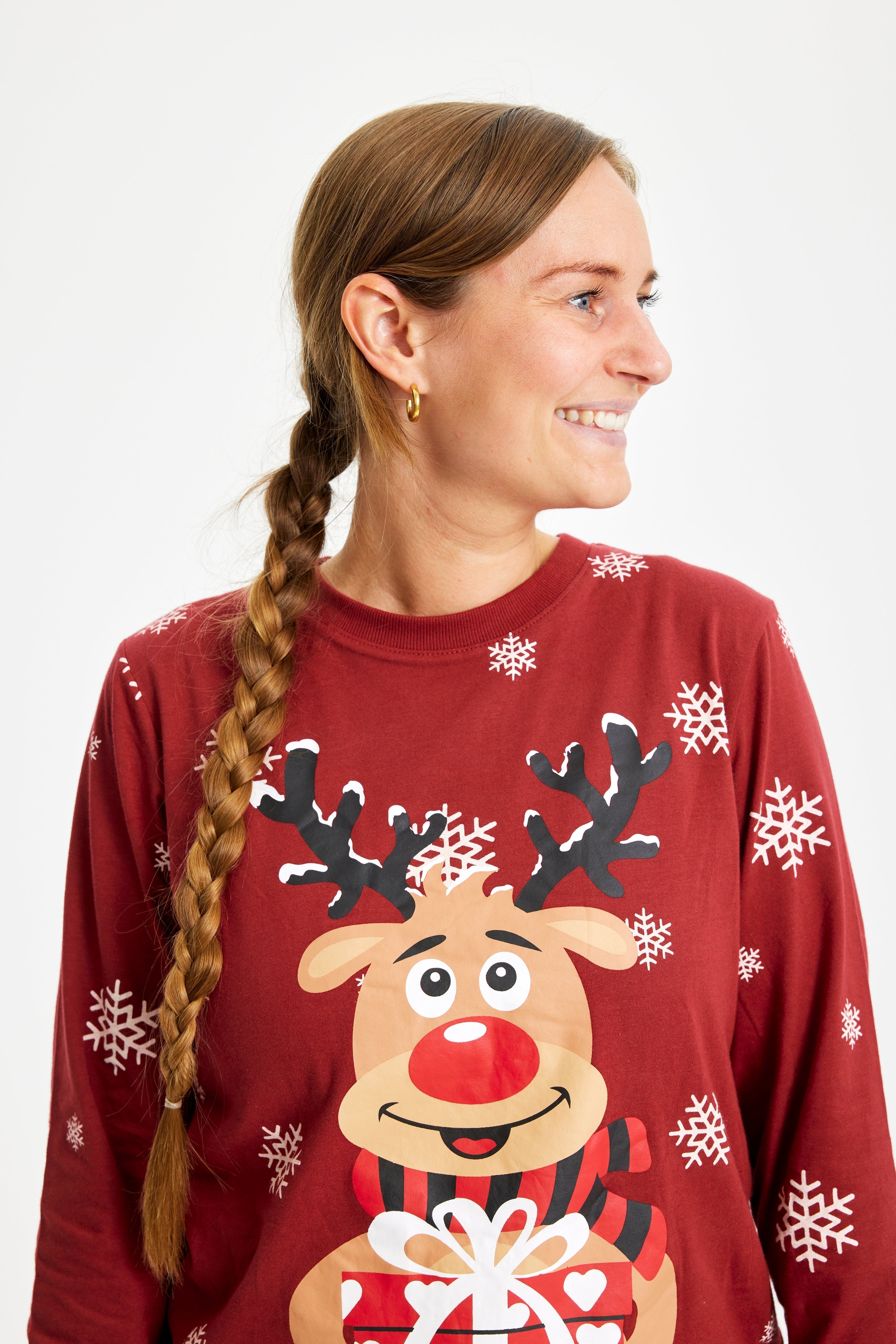 Een vrouw opzij kijkend in een rode kerstpyjama met Rudolph erop.
